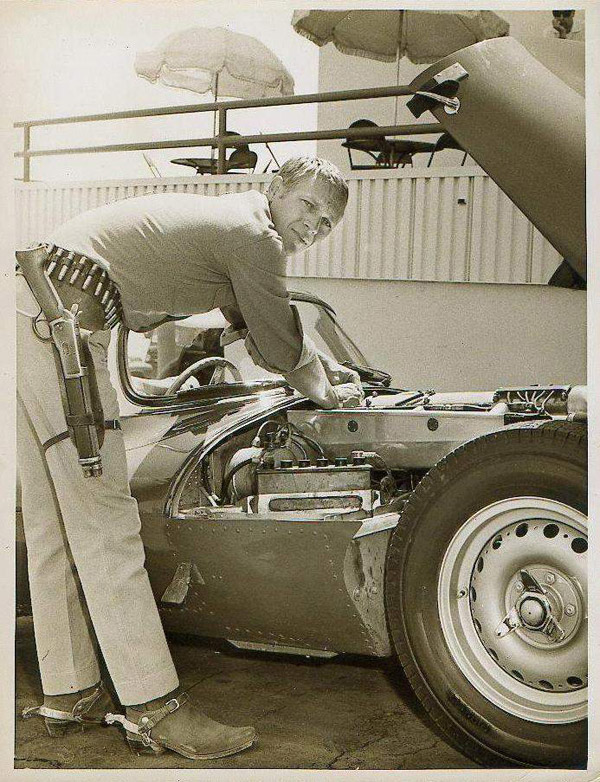 Steve McQueen les mains dans le moteur de sa Jaguar XK SS, en tenue de "Josh Randall" de la série "Au Nom de la loi" 